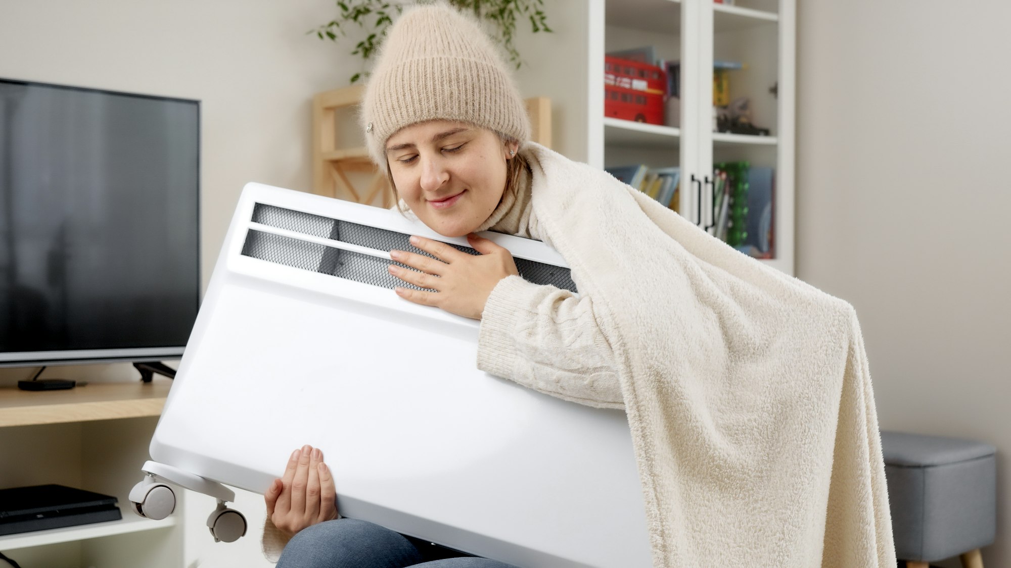 Young woman embracing electric heater in her flat with heating problems. Concept of energy crisis